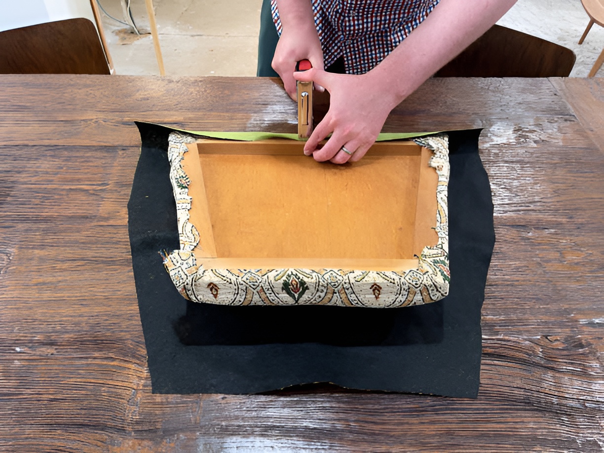 man stapling new fabric over a seat frame without removing old fabric